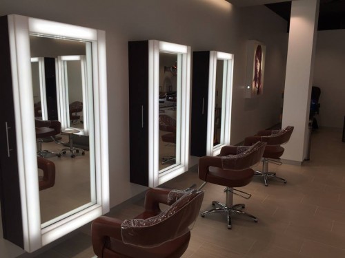 A modern hair salon with brown swivel chairs and large rectangular mirrors framed with lights along the wall. - Nuovo Salon Group in Sarasota & Bradenton, FL