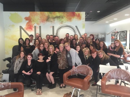 A large group of people posing and smiling together inside a modern salon with a colorful "NUOVO" sign on the wall behind them. - Nuovo Salon Group in Sarasota & Bradenton, FL
