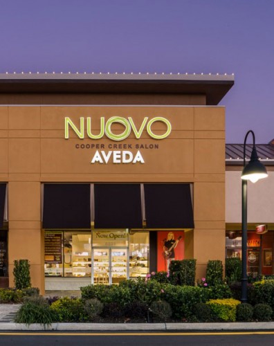 Exterior view of NUOVO Cooper Creek Salon Aveda storefront with illuminated signage, large windows, and landscaped greenery in front. - Nuovo Salon Group in Sarasota & Bradenton, FL