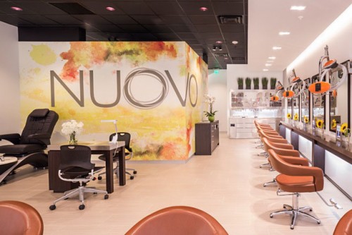 Modern salon interior with brown chairs, styling stations, and a wall featuring the word "NUOVO" on a colorful background. Manicure and pedicure stations are visible on the left. - Nuovo Salon Group in Sarasota & Bradenton, FL