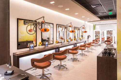 Modern hair salon interior with brown styling chairs, mirrors, and hairdryers arranged in a row along a well-lit counter. - Nuovo Salon Group in Sarasota & Bradenton, FL