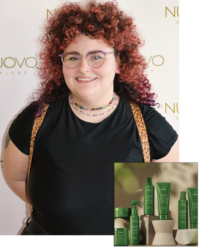 A person with curly red hair, glasses, and a black shirt stands in front of a "Nuovo Salons" backdrop; inset shows green bottles of Aveda hair care products. - Nuovo Salon Group in Sarasota & Bradenton, FL