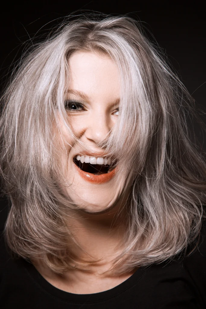A person with shoulder-length blonde hair laughing with their mouth wide open. - Nuovo Salon Group in Sarasota & Bradenton, FL